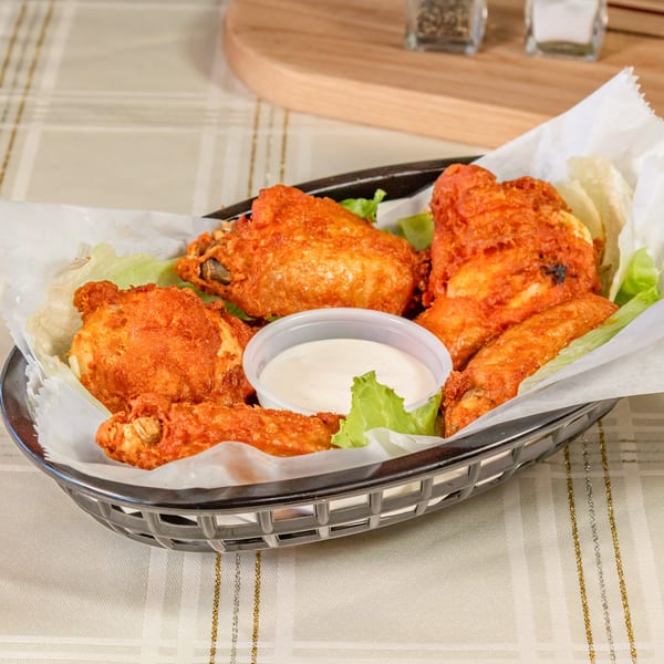 A basket of crispy, orange-glazed chicken wings with a side of ranch dressing and lettuce.