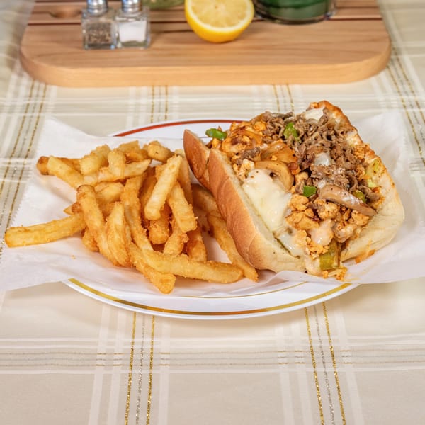A Philly cheesesteak with melted cheese, onions, and peppers, served with golden french fries.