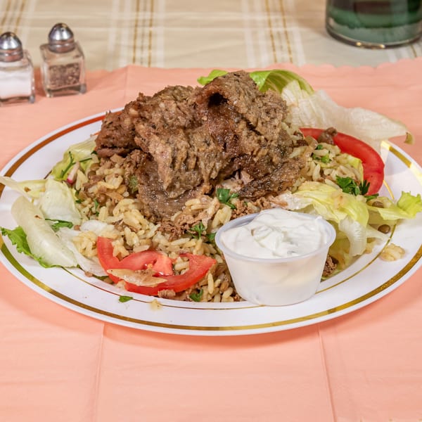 A plate of rice and lentils topped with seasoned meat, lettuce, tomatoes, and a side of white sauce.