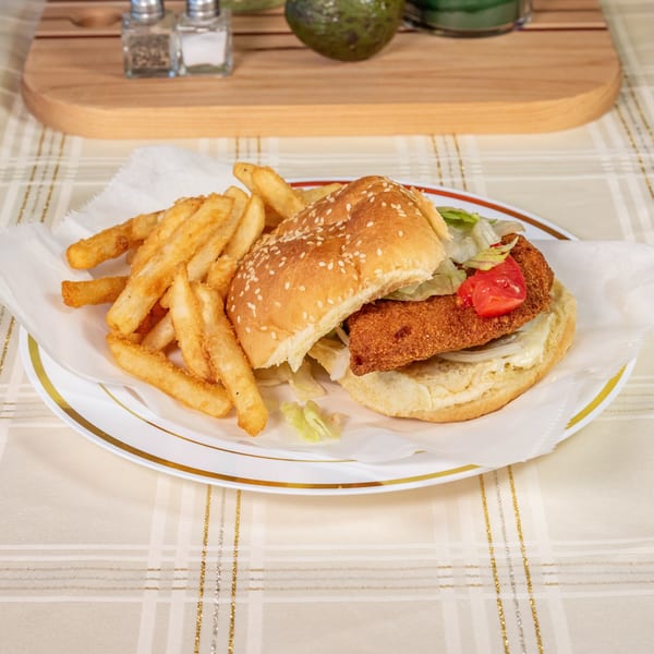A fried fish sandwich with lettuce, tomato, onion, and mayonnaise, served with french fries.